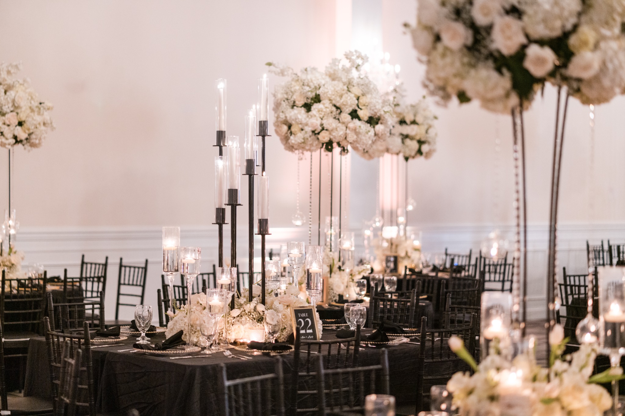 Black reception tables layered with white floral centerpieces, gold accents and glowing candles