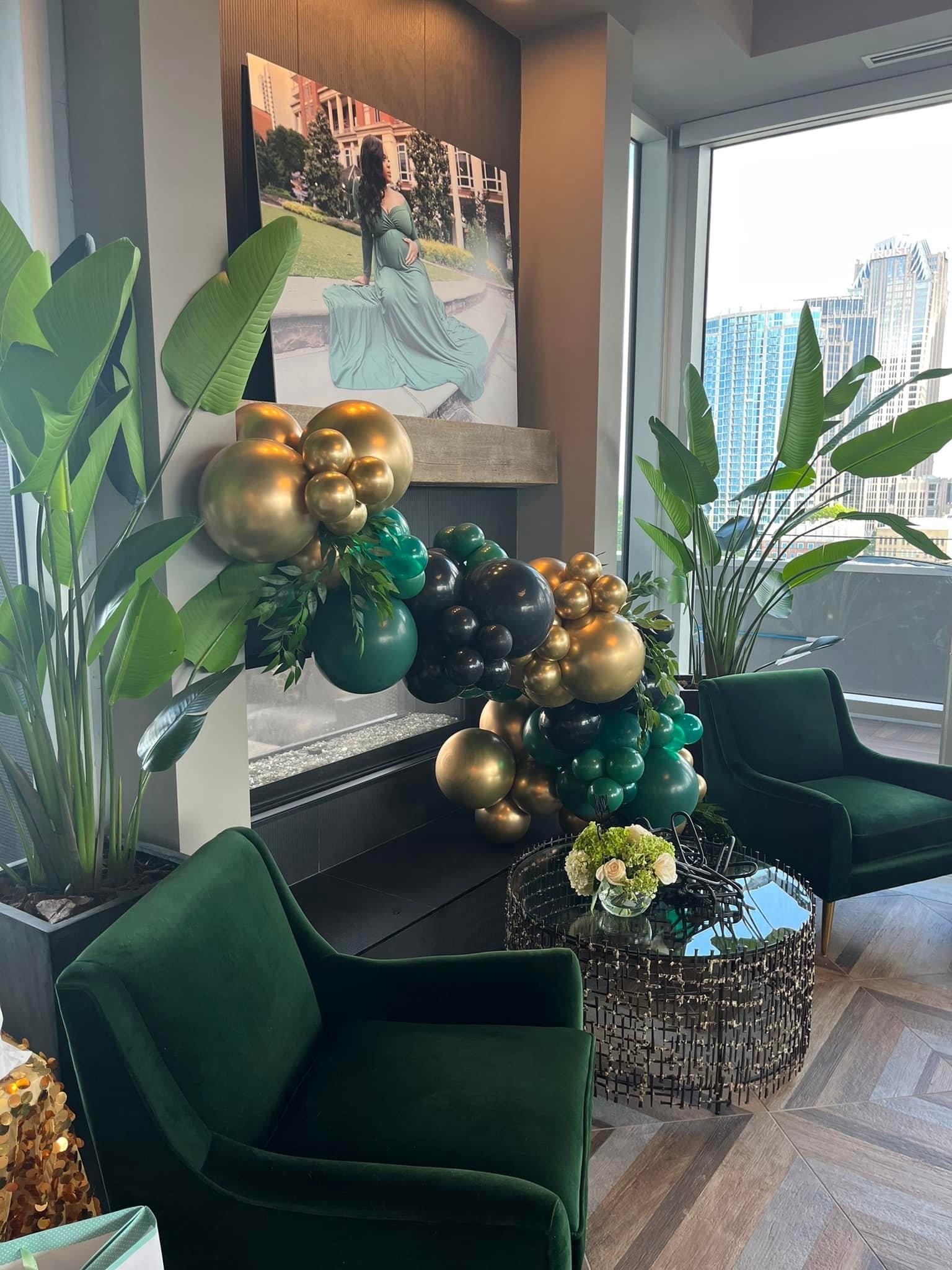 Emerald velvet lounge chairs and a mirrored floral table beside a black, green and gold balloon installation
